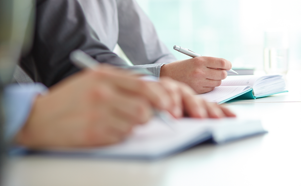 hands close up of two coworkers writing in notebooks