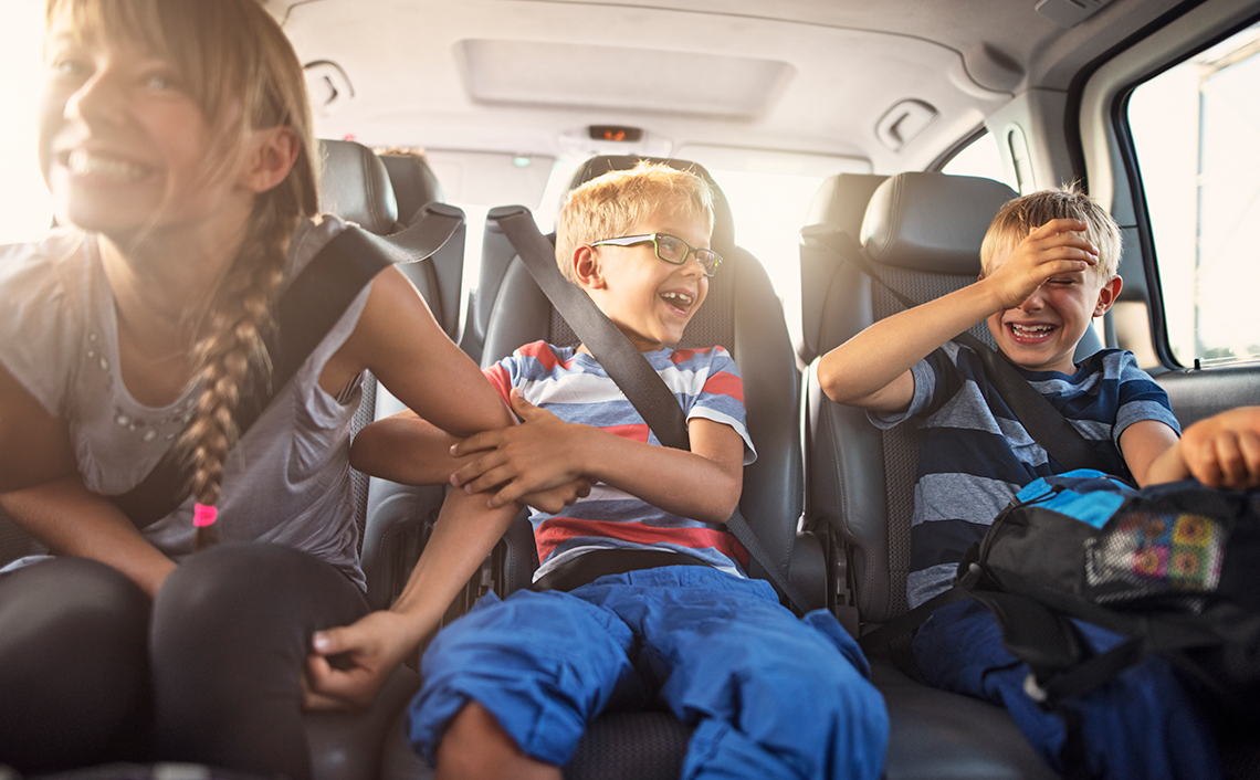 three kids sitting in the backseat of a car laughing with seatbelts on