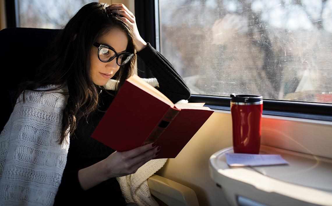woman reading a book in a train next to a window