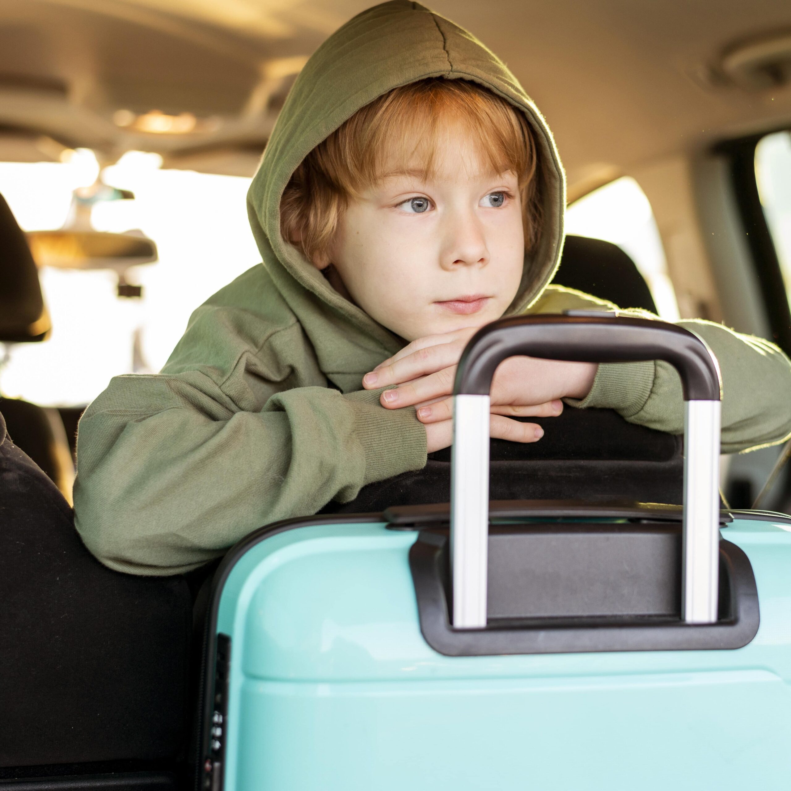 Front view of young child in the backseat of a car with some luggage